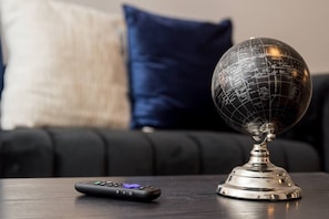 Ein Globus auf einem Metallständer, eine Fernbedienung und ein dunkelgraues Sofa mit Kissen im Hintergrund.