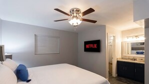 A bedroom with a bed, a ceiling fan, a wall-mounted TV displaying 'NETFLIX,' and a bathroom with a mirror and sink. - King SIze 🛏 Fast WiFi 📶Central Workspace & Cozy✅ (McAllen)
