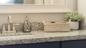 A bathroom vanity with a granite countertop, a mirror, a faucet, a soap dispenser, and a woven basket. - King SIze 🛏 Fast WiFi 📶Central Workspace & Cozy✅ (McAllen)