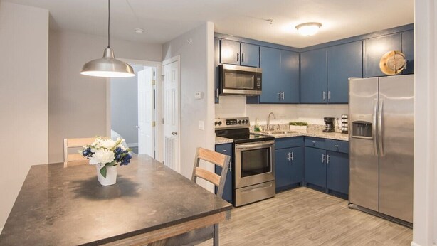 A modern kitchen with blue cabinets, stainless steel appliances, and a dining area with a table and chairs. - King SIze 🛏 Fast WiFi 📶Central Workspace & Cozy✅ (McAllen)