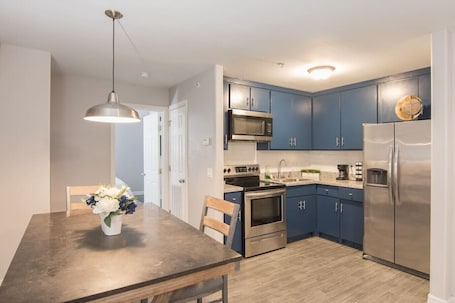 A modern kitchen with blue cabinets, stainless steel appliances, a dining table with chairs, and a pendant light.. King SIze 🛏 Fast WiFi 📶Central Workspace & Cozy✅