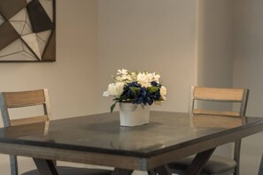 A dining table with a floral centerpiece, two wooden chairs, and a geometric wall art piece.