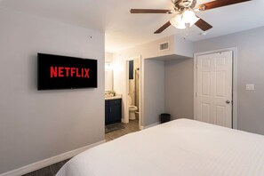 A bedroom with a bed, a ceiling fan, a TV mounted on the wall, and a door leading to a bathroom.