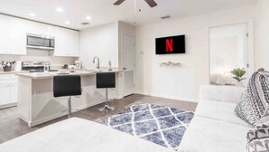 Una cucina moderna con forno a microonde, piano cottura e sgabelli da bar. Si nota una ventola a soffitto, una TV montata a parete e un tappeto decorato a pavimento.