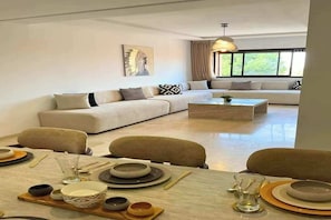 A modern living room with a sofa, dining table set, and a large window. - Luxury 3BR Residence - Gueliz - Pool-Walk to Majorelle (Marrakech)