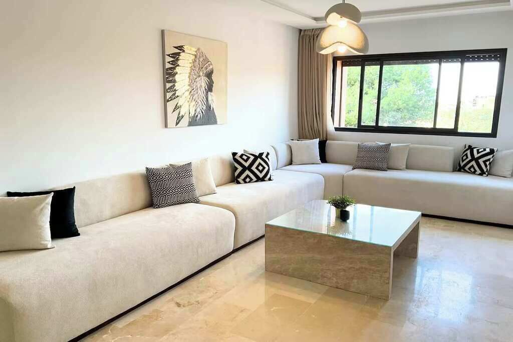 A living room with a beige sofa, patterned cushions, a glass coffee table, and a Native American feather artwork on the wall.
