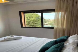 A hotel room with a bed, a window with a view of greenery, and a curtain. - Luxury 3BR Residence - Gueliz - Pool-Walk to Majorelle (Marrakech)