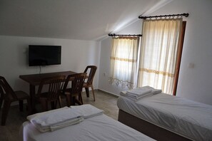 A room with two beds, a table with chairs, a television, and curtains.