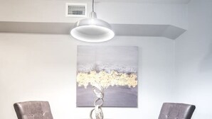 Een eetgedeelte met een ronde tafel, vier stoelen, een hanglamp en een schilderij aan de muur.