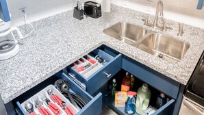 Een keuken met granieten aanrechtbladen, een dubbele spoelbak en een inbouw ladeorganizer met keukengerei en schoonmaakmiddelen.