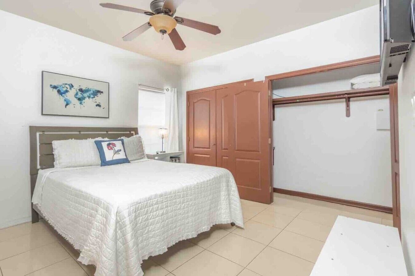 A bedroom with a bed, a ceiling fan, a wardrobe, and a world map on the wall.