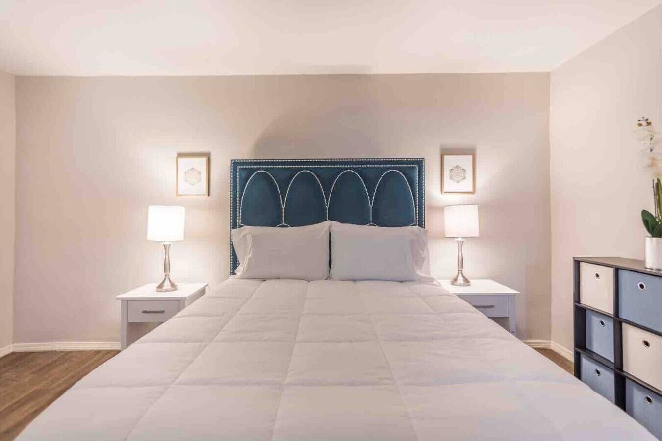 A bedroom with a large bed, two bedside tables, a headboard, and a nightstand with a lamp.