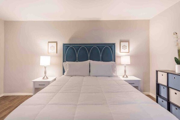 A bedroom with a large bed, two bedside tables, a headboard, and a nightstand with a lamp.