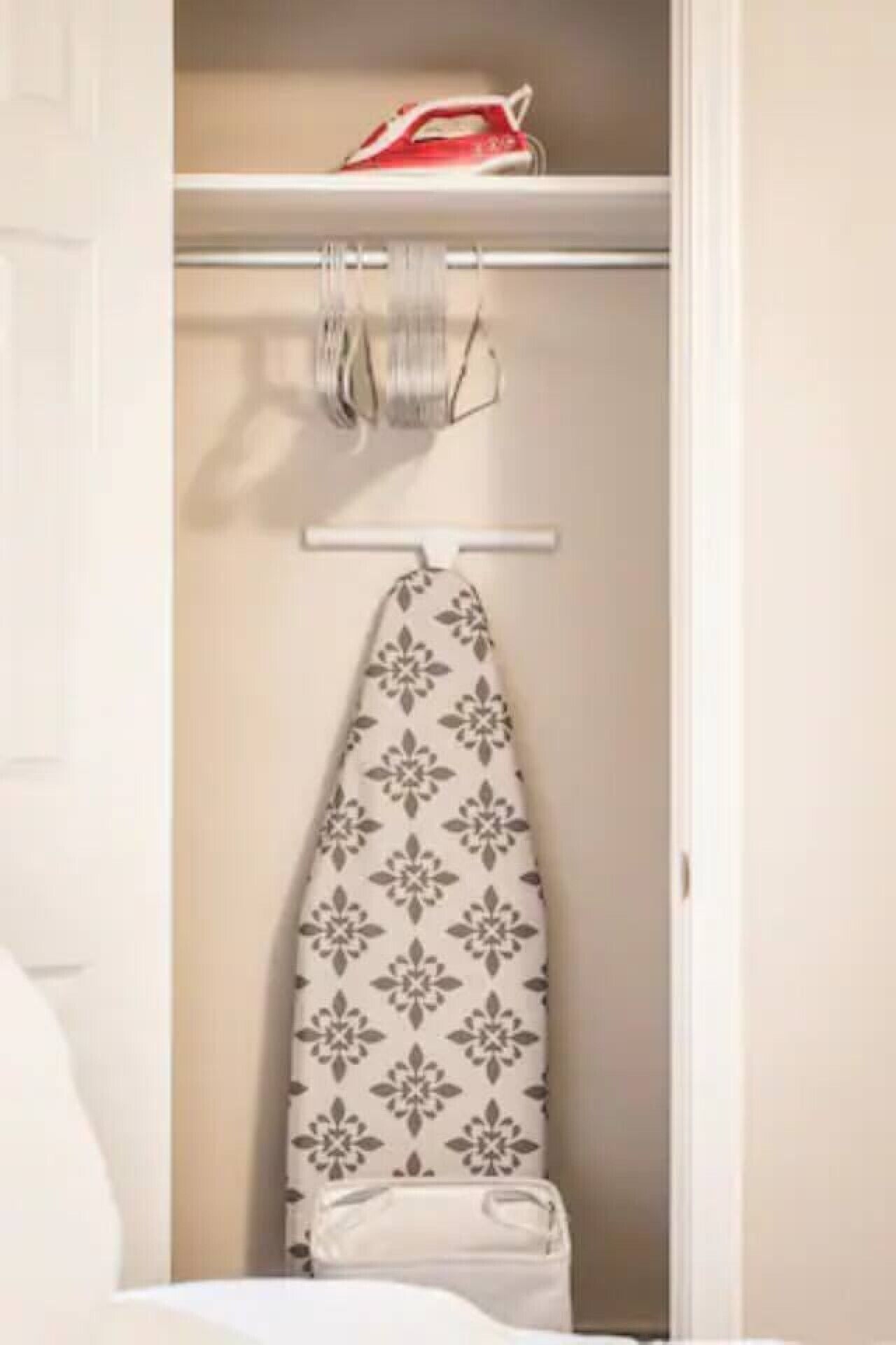 A closet with an ironing board, a hanging rack, and a white bag.