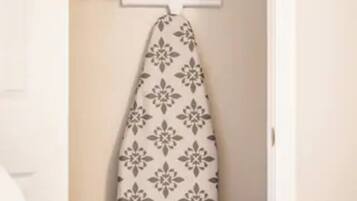 A closet with an ironing board, a hanging rack, and a white bag.