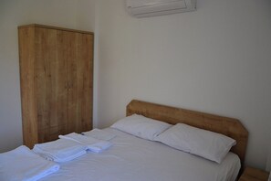 A single bed with white linens and pillows, a wooden wardrobe, and a wall-mounted air conditioning unit.
