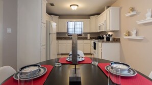 Une cuisine moderne avec des meubles blancs, une table à manger pour quatre personnes et une vue sur l’espace repas.