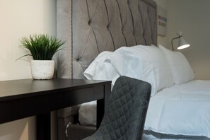 Ein ordentlich eingerichtetes Hotelzimmer mit einem Bett, einem Nachttisch mit Topfpflanze, einem Sessel und einer Lampe.