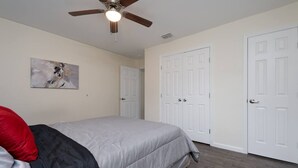 Ein Schlafzimmer mit einem Bett, einem Deckenventilator, einer Tür und einem Bild an der Wand.