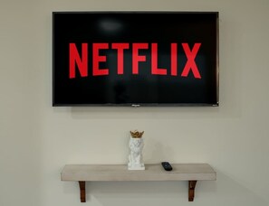 Een televisie bevestigd aan een muur, met het woord 'NETFLIX' in rode letters. Daaronder een wit beeld met een gouden kroon op een houten plank.
