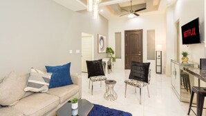 Uma sala de estar moderna com um sofá, poltronas, uma mesa de centro, uma TV e um ventilador de teto.