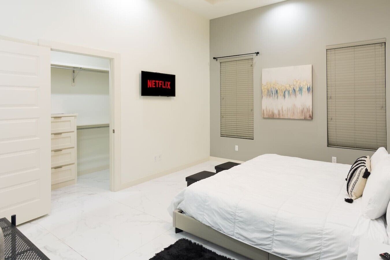 A bedroom with a bed, a closet, a wall-mounted TV, and a window with blinds.