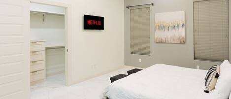 A bedroom with a bed, a closet, a wall-mounted TV, and a window with blinds.