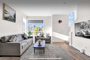 Ein modernes Wohnzimmer mit einem grauen Sofa, einem Couchtisch und einem großen Fenster.