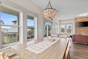 A spacious dining area with a long table, a woven rug, and a modern chandelier. - Pool, Putting Green, Boat Parking, Giant Sand Pit, Steps to Beach (Port St. Joe)