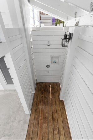 A narrow hallway with white paneling and wooden flooring, leading to a door with a small window and a lantern.