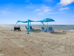 Ein Strand mit Sonnensegel, Liegestühlen und einem Wagen.