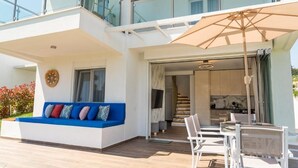 Ein modernes, zweistöckiges Gebäude mit Balkon, Sitzgelegenheit im Freien und einer Treppe, die zu einem Innenraum führt.