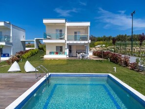Una casa moderna de dos pisos con piscina, mobiliario exterior y un jardín cuidado.