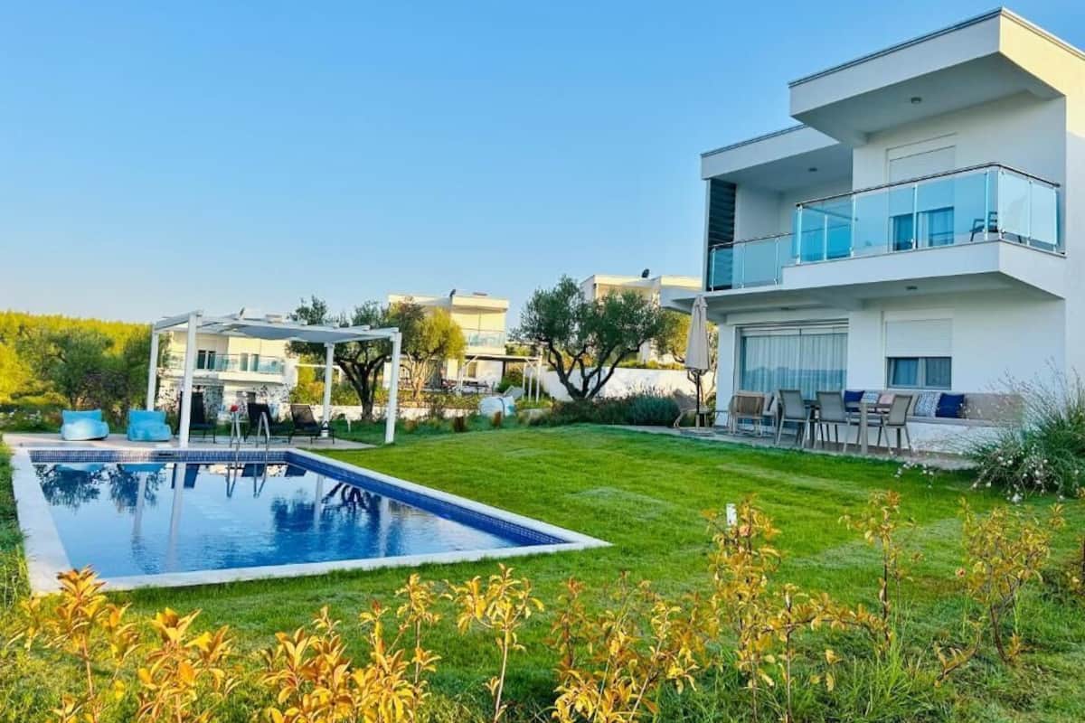 Une maison moderne à deux étages, dotée d’une piscine, d’un patio couvert et d’une pelouse bien entretenue.