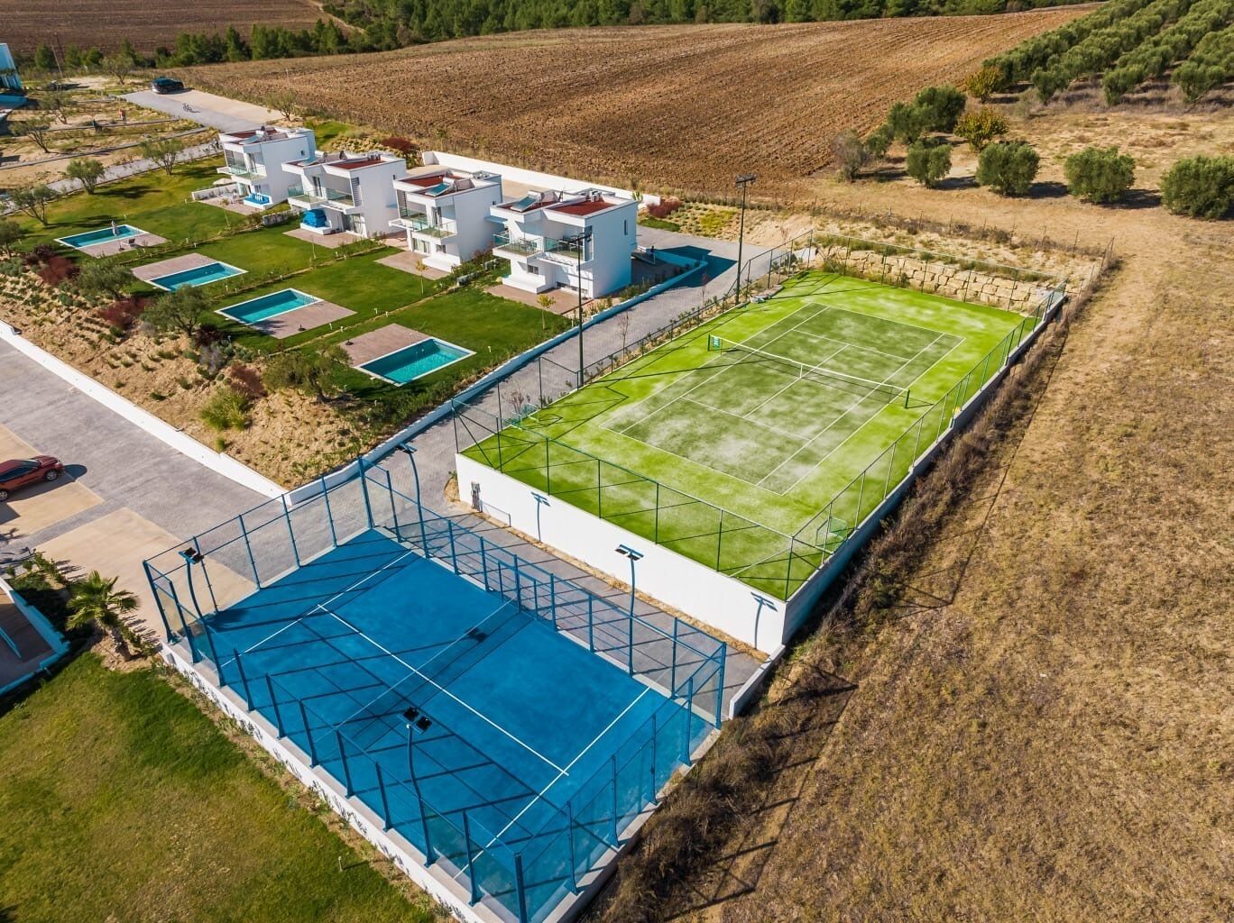 A modern residential complex with multiple houses, a tennis court, and a swimming pool.