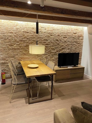 Ein Essbereich mit Holztisch und Stühlen, einem Fernseher auf einem Holzgestell und einer Wand aus Stein.