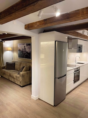 Eine moderne Küche mit integriertem Kühlschrank, Backofen und Mikrowelle. Im angrenzenden Wohnbereich befindet sich eine Couch und eine Lampe.
