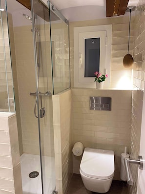 Ein Badezimmer mit Duschkabine, Toilette und kleinem Fenster mit einer Blume.