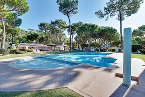 Ein Swimmingpool mit Liegestühlen, umgeben von Bäumen und einem Gebäude im Hintergrund.