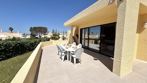 A patio with a table set for six, surrounded by chairs, with a view of the sea and buildings in the background. - Vilamoura Golf Villa 4 by Homing (Loulé)