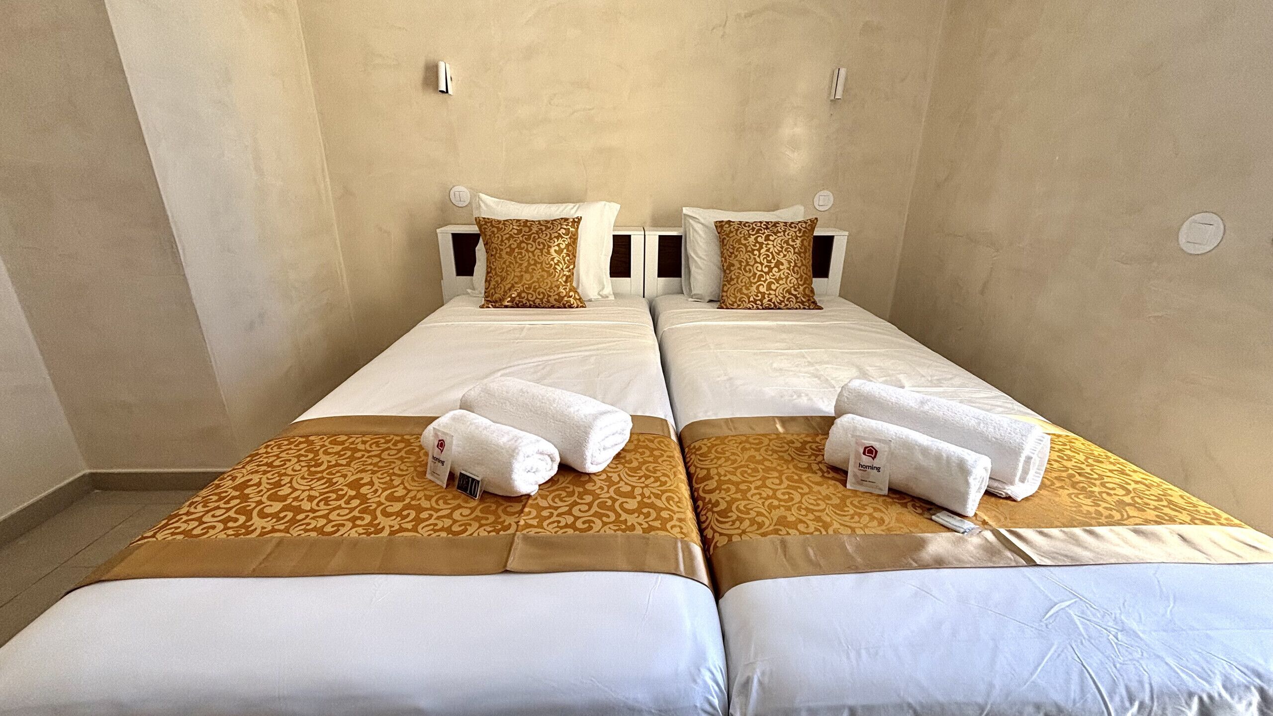 A hotel room with two beds, each with a patterned bedspread, white linens, and a matching pillow. There are two white towels on each bed.