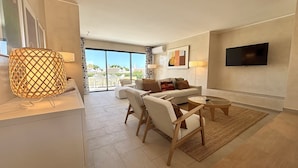 A modern living room with a sofa, chairs, a coffee table, and a TV mounted on the wall. - Vilamoura Golf Villa 4 by Homing (Loulé)