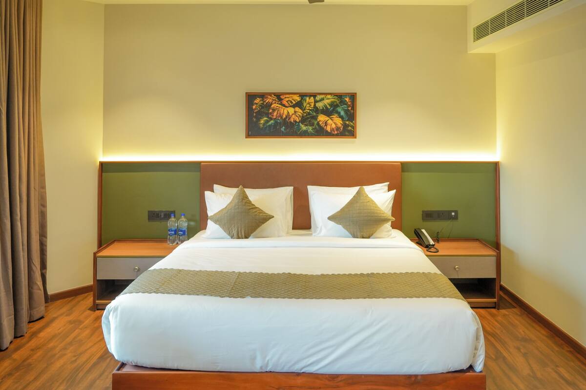 A hotel room with a large bed, two bedside tables, a wall-mounted painting, and a power outlet.