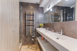 Un baño moderno con cabina de ducha de vidrio, un lavamanos blanco con un solo grifo y un espejo grande.