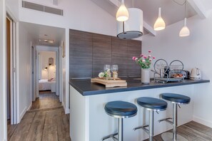 Une cuisine moderne dotée d’un îlot central, de tabourets de bar, de luminaires suspendus et donnant sur la chambre adjacente.