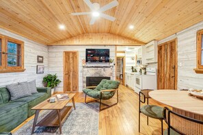 Interior acollidor d'una cabana amb sostre de fusta, una llar de foc, zona de dinar i cuina.