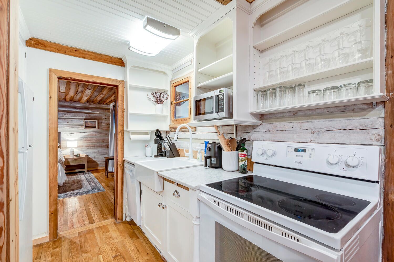 A compact kitchen with a microwave, stove, and shelves with glass jars.