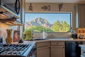 Eine Küche mit Herd, Spüle und Geschirrspüler, ein großes Fenster mit Blick auf die Berge sowie dekorative Wandelemente.
