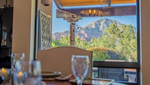 A dining table with a view of mountains through a window. - Luxury Sedona Views, Spa, Sauna, Cold Plunge (Sedona)