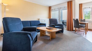 Et moderne hotelværelse med sofa, lænestol, spisebord og udsigt til det fri.